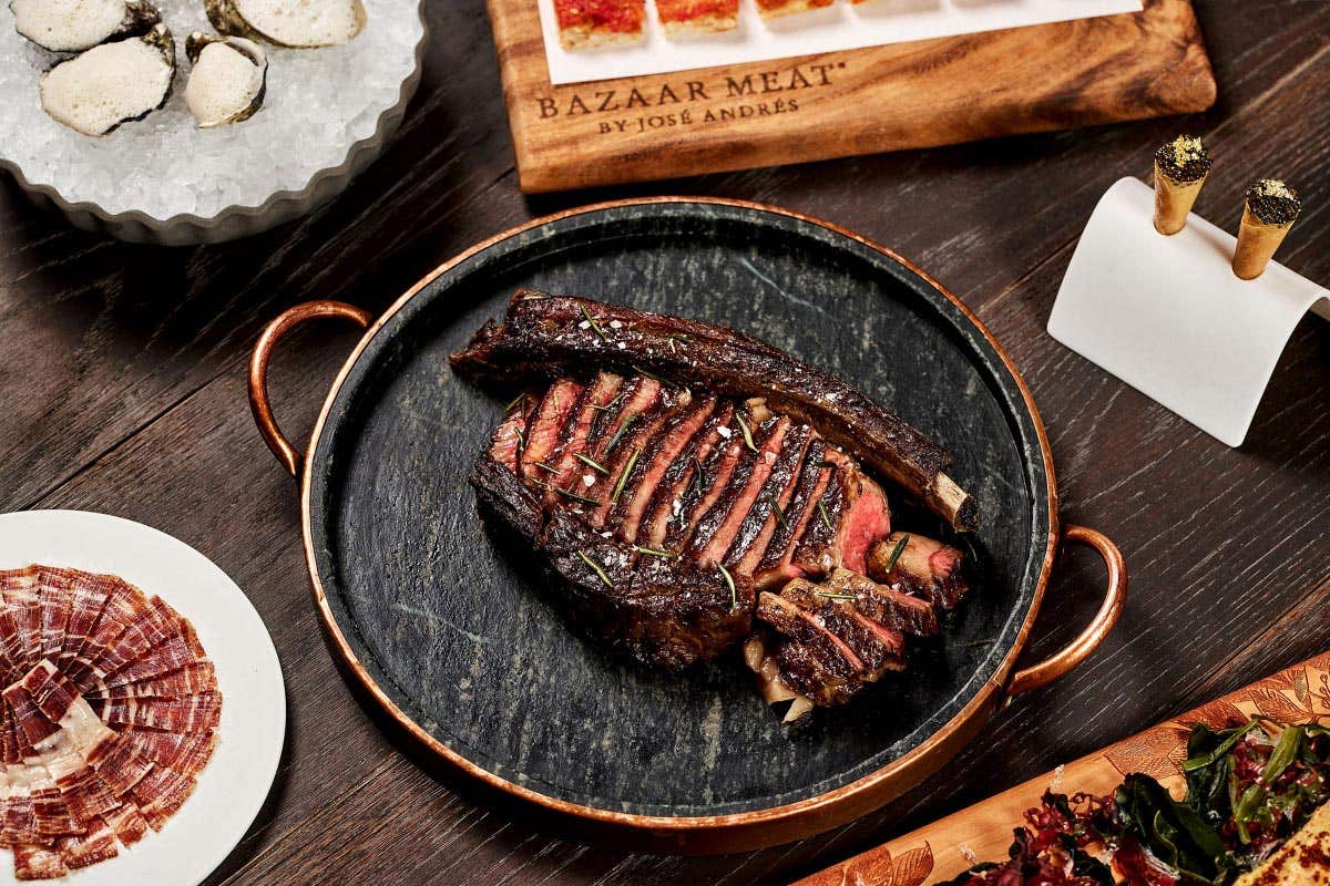 A variety of gourmet dishes featuring a sliced steak, oysters, bread with spread, crispy cones, and cured meat.