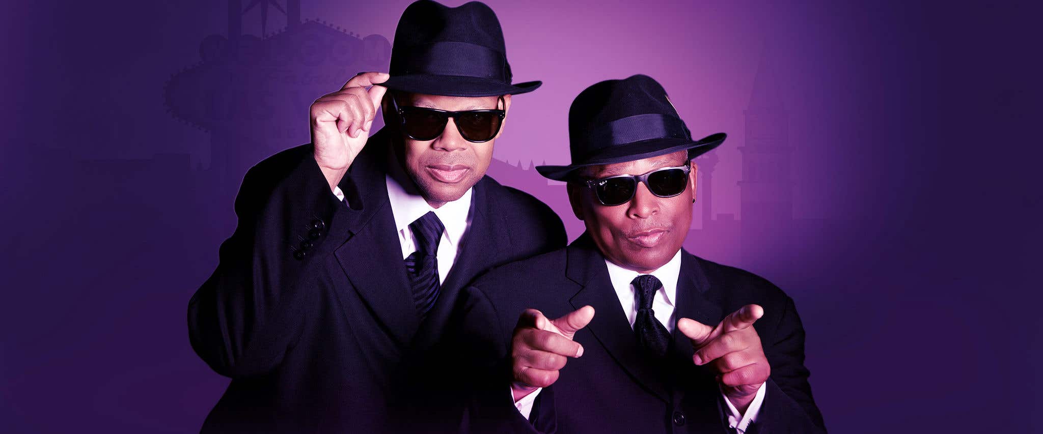 Jimmy Jam and Terry Lewis in black hat, dark sunglasses, white shirt, black tie and black jacket looking at the camera.