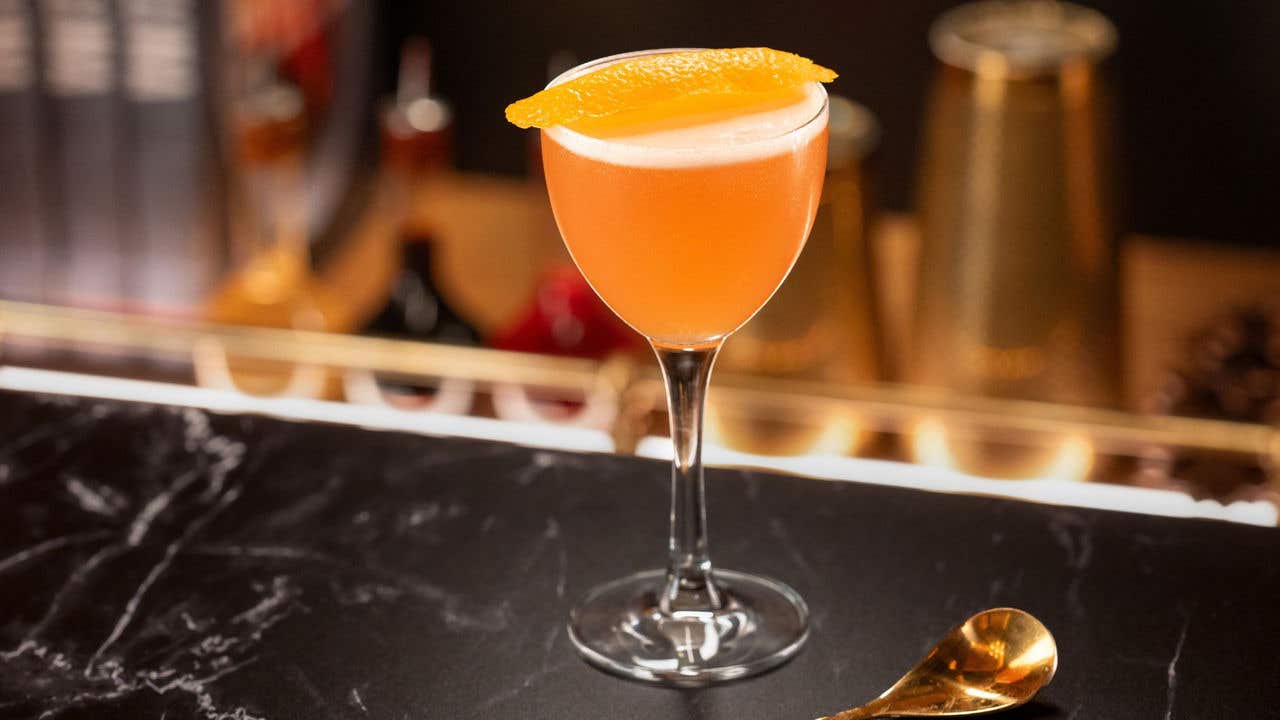 Pink cocktail garnished with an orange peel.