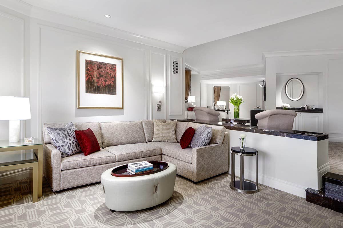 Spacious living room with beige sectional sofa, red and gray cushions, round ottoman, modern decor, and soft lighting.