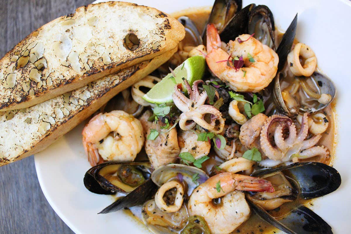 A seafood dish with shrimp, mussels, squid, and lime, served with two slices of toasted bread.