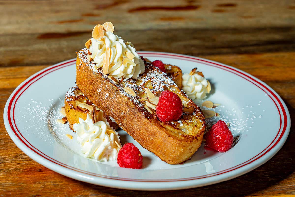 Pieces of French toast topped with sliced almonds, raspberries, butter and powder sugar. 