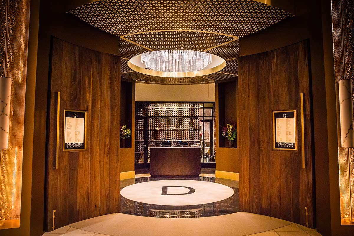 Luxurious restaurant entrance with wooden double doors, menu displays, circular lighting feature, and stylish interior.