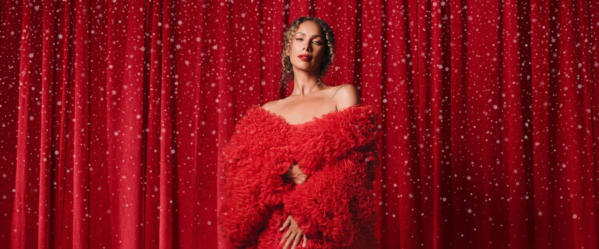 Leona Lewis in red dress in front of red curtain background with snow falling all around her. 