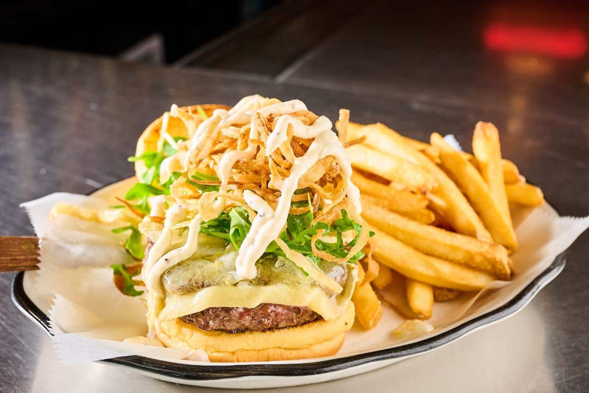 Cheeseburger stacked with cheese, lettuce, crispy onions and sauce with a side of fries.