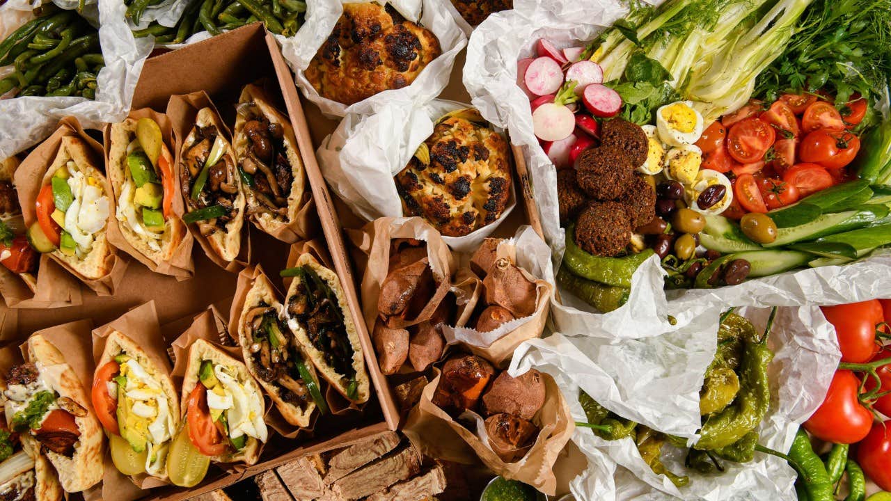 An assortment of Middle Eastern food including stuffed pita sandwiches, falafel, roasted vegetables, and fresh greens.