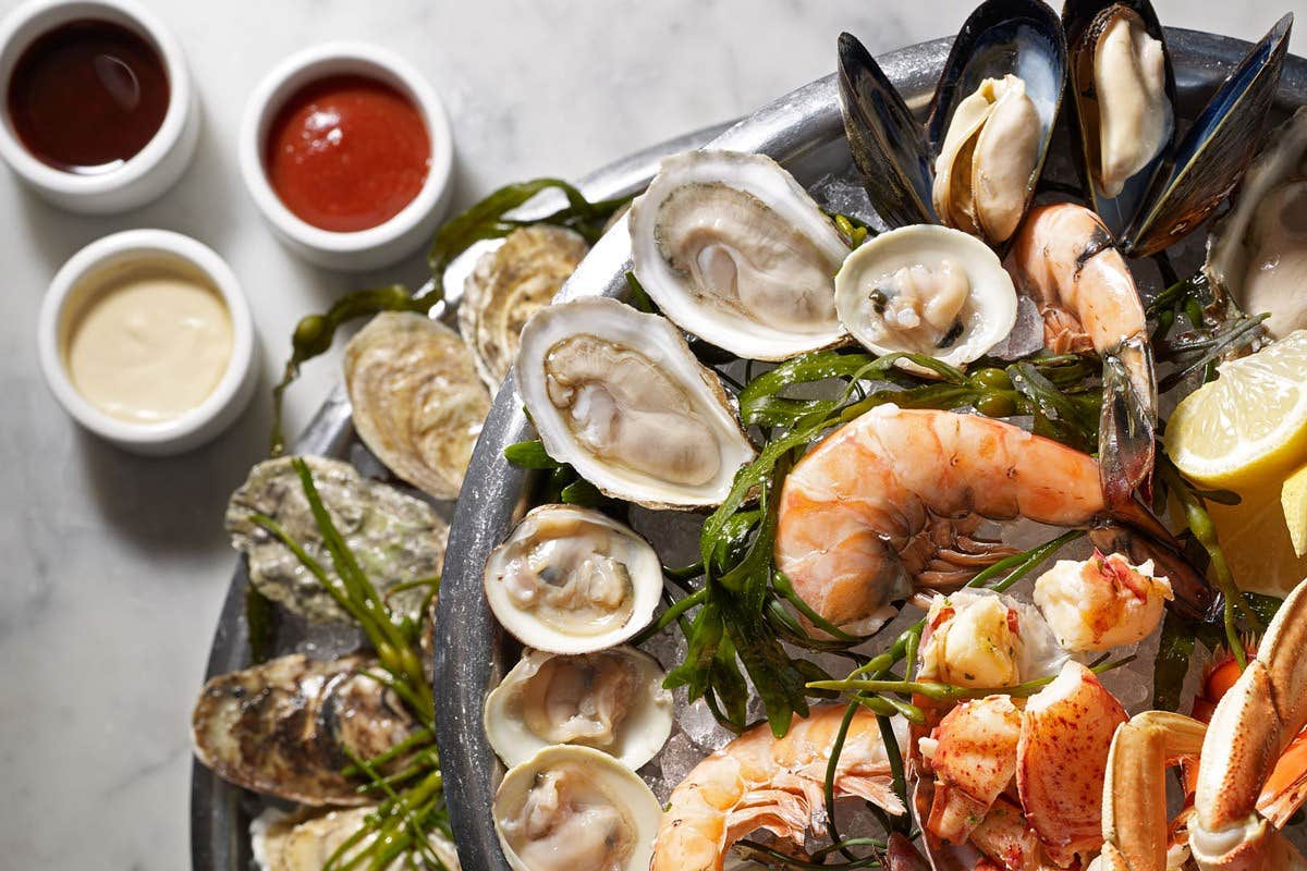 A seafood platter with shrimp, clams, oysters, mussels, and lobster, accompanied by lemon wedges and dipping sauces.