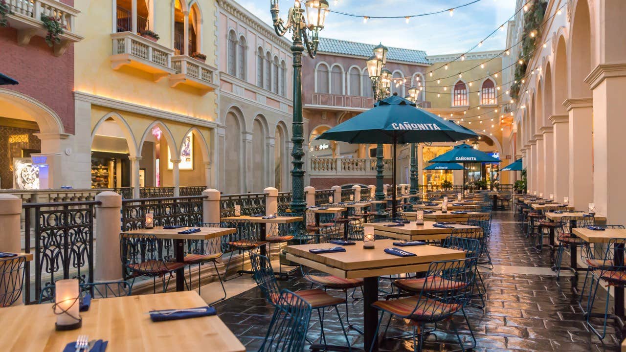 Outdoor restaurant with tables and chairs set under string lights and parasols, surrounded by European-style buildings.