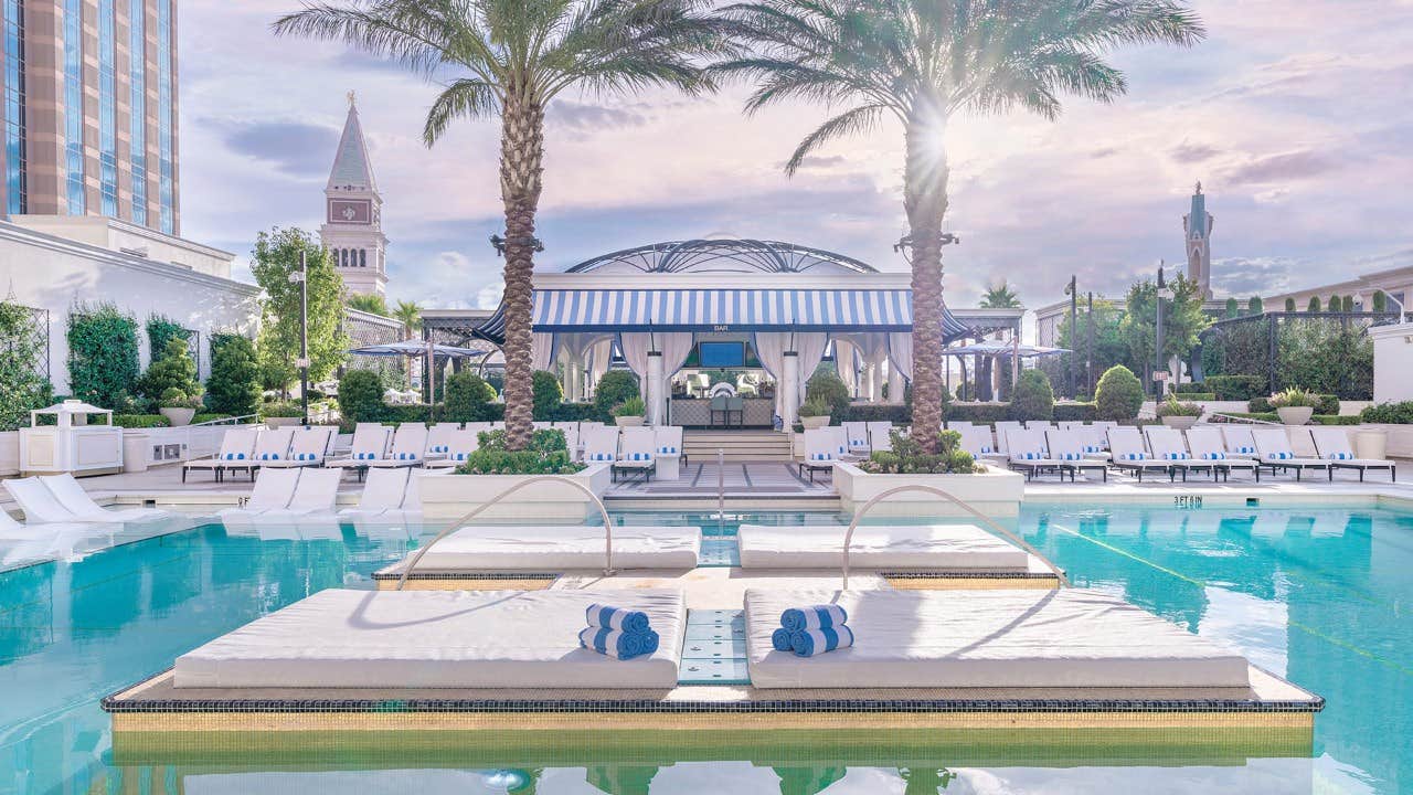 Luxurious poolside area with lounge beds, palm trees, and a cabana under a dome-like structure on a sunny day.