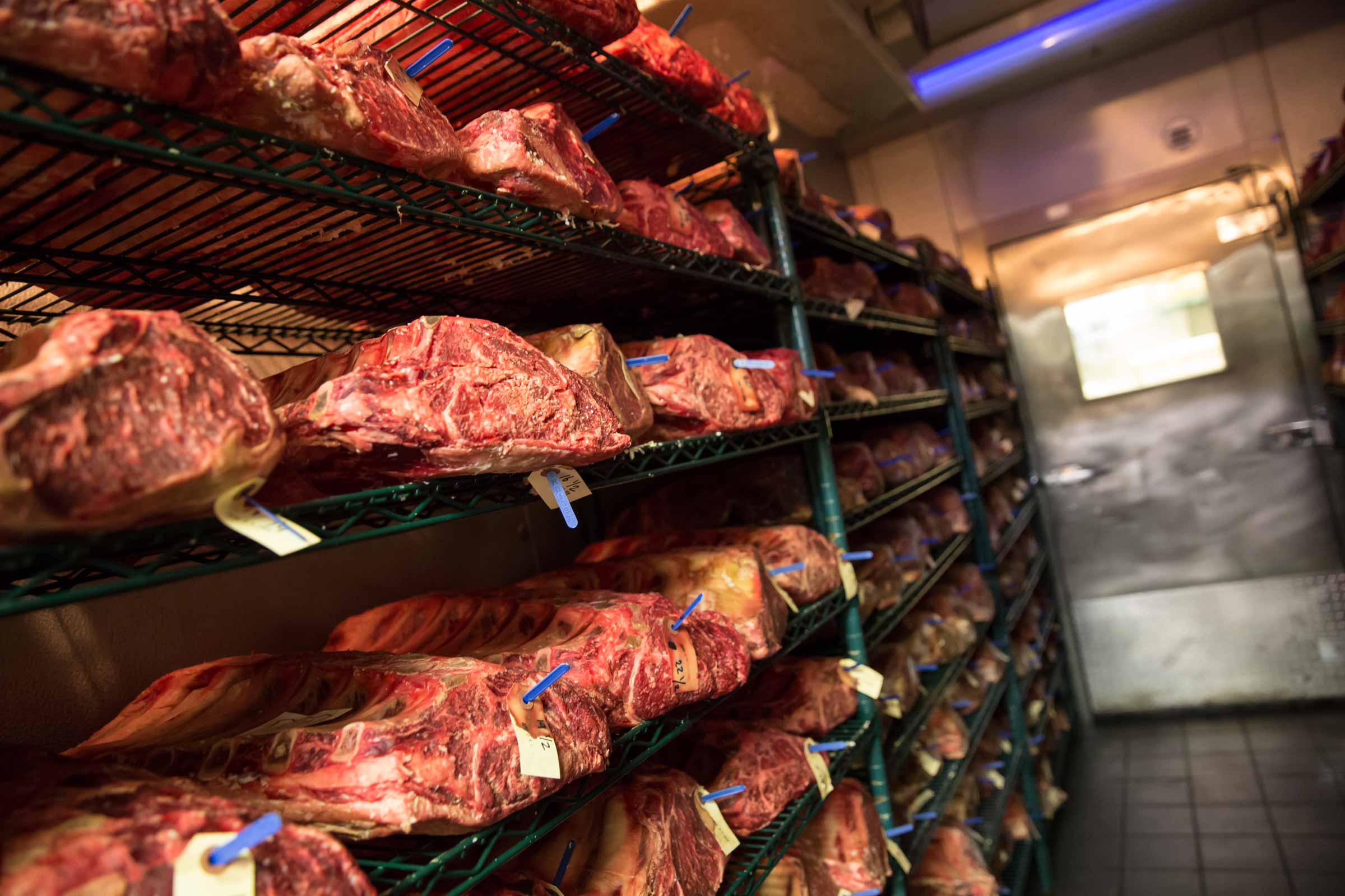 A storage room with multiple shelves filled with large cuts of meat, likely aging or being stored for future use.