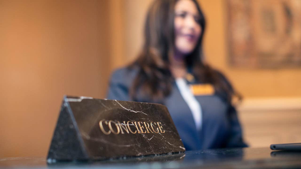 Concierge sign on a counter with an out-of-focus woman in a suit standing in the background.