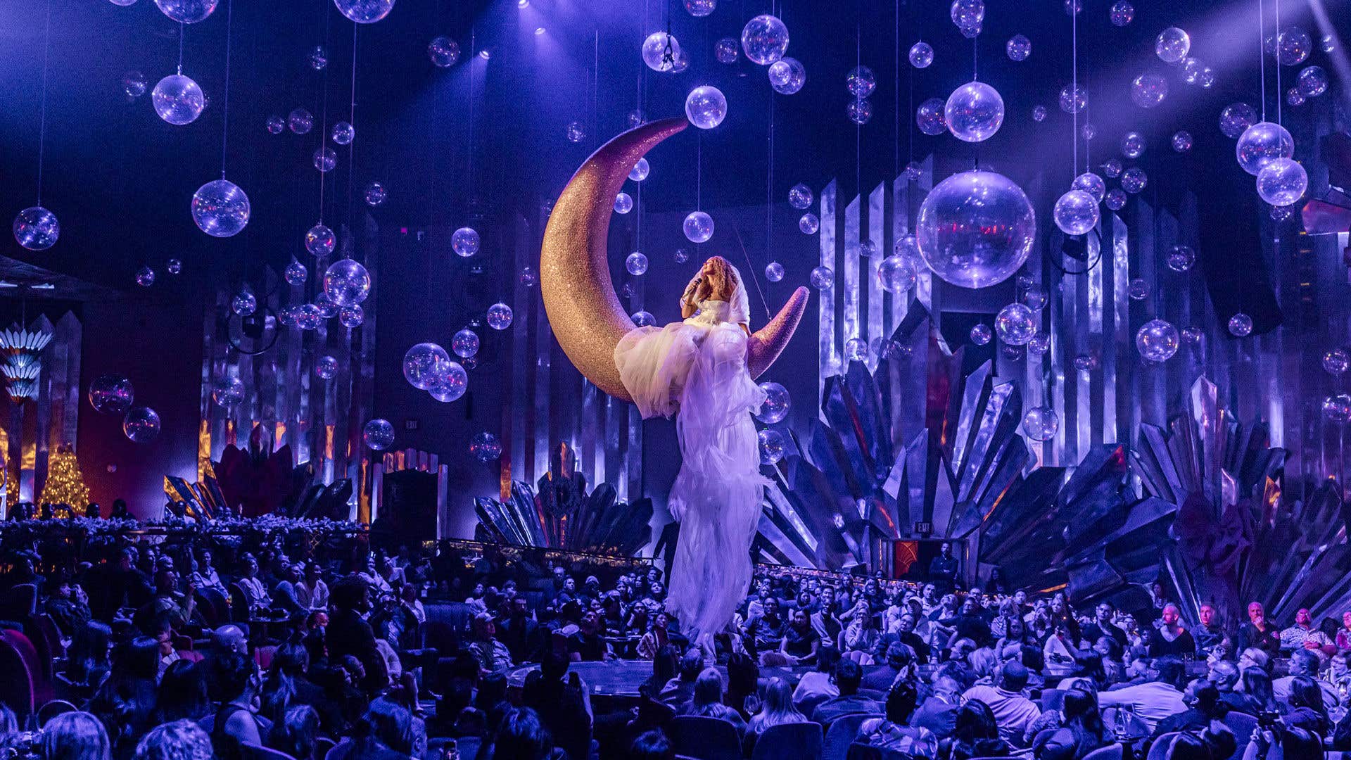 Leona Lewis suspended above the audience on a large gold crescent moon prop surrounded by floating glass orbs during the A Starry Night show at Voltaire.