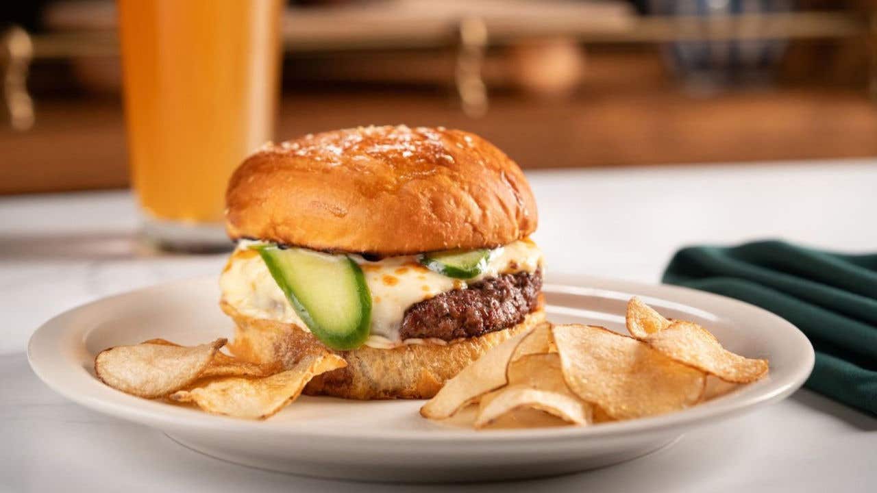 Cheeseburger with pickles on a bun, served with potato chips.