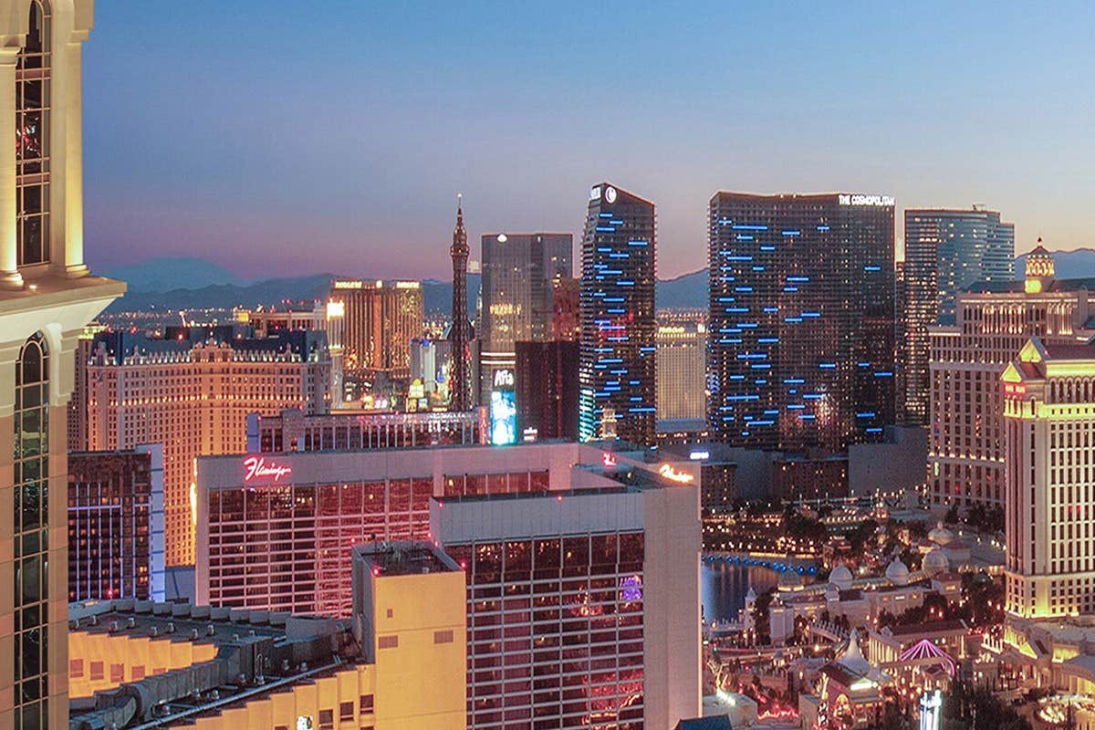 Las Vegas Strip at dusk with illuminated buildings, casinos, and hotels against a backdrop of mountains and twilight sky.