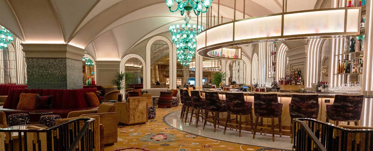 Elegant bar with arched ceiling, green chandeliers, and plush seating featuring a semi-circular bar counter.