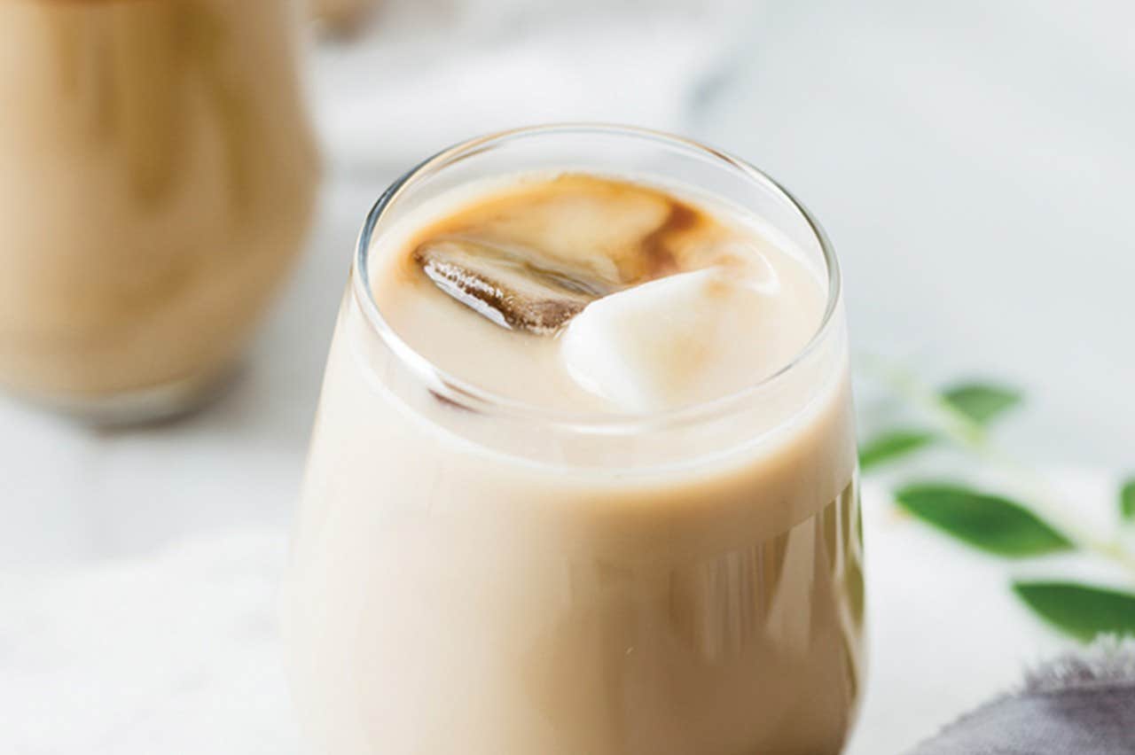 A close-up of a glass filled with iced coffee, showing ice cubes and creamy mixed layers.