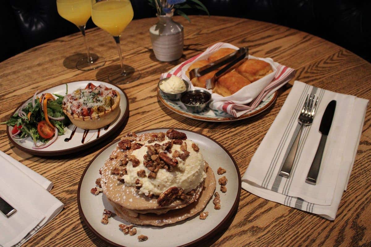 Brunch table with stacked pancakes, biscuits, sides, and drinks on a wooden tabletop.
