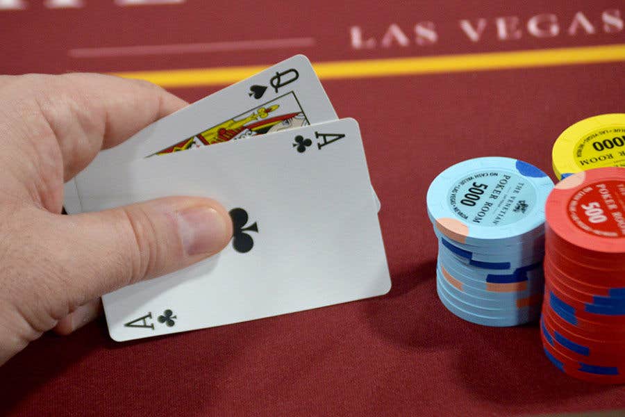 A hand holding an Ace and a Queen at a poker table