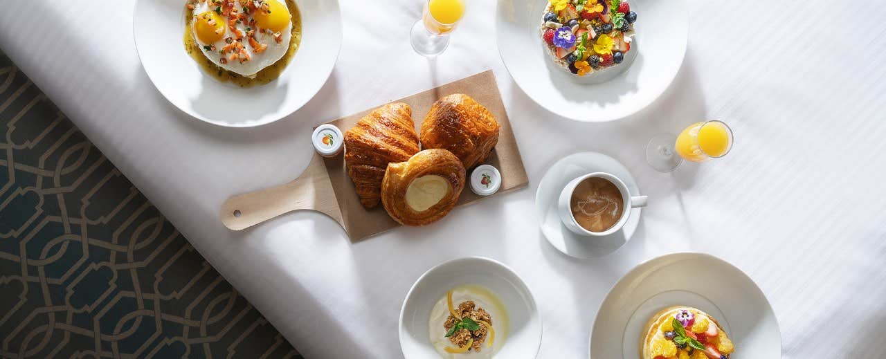 A breakfast spread with eggs, pastries, fruit, coffee, and orange juice on a white tablecloth.