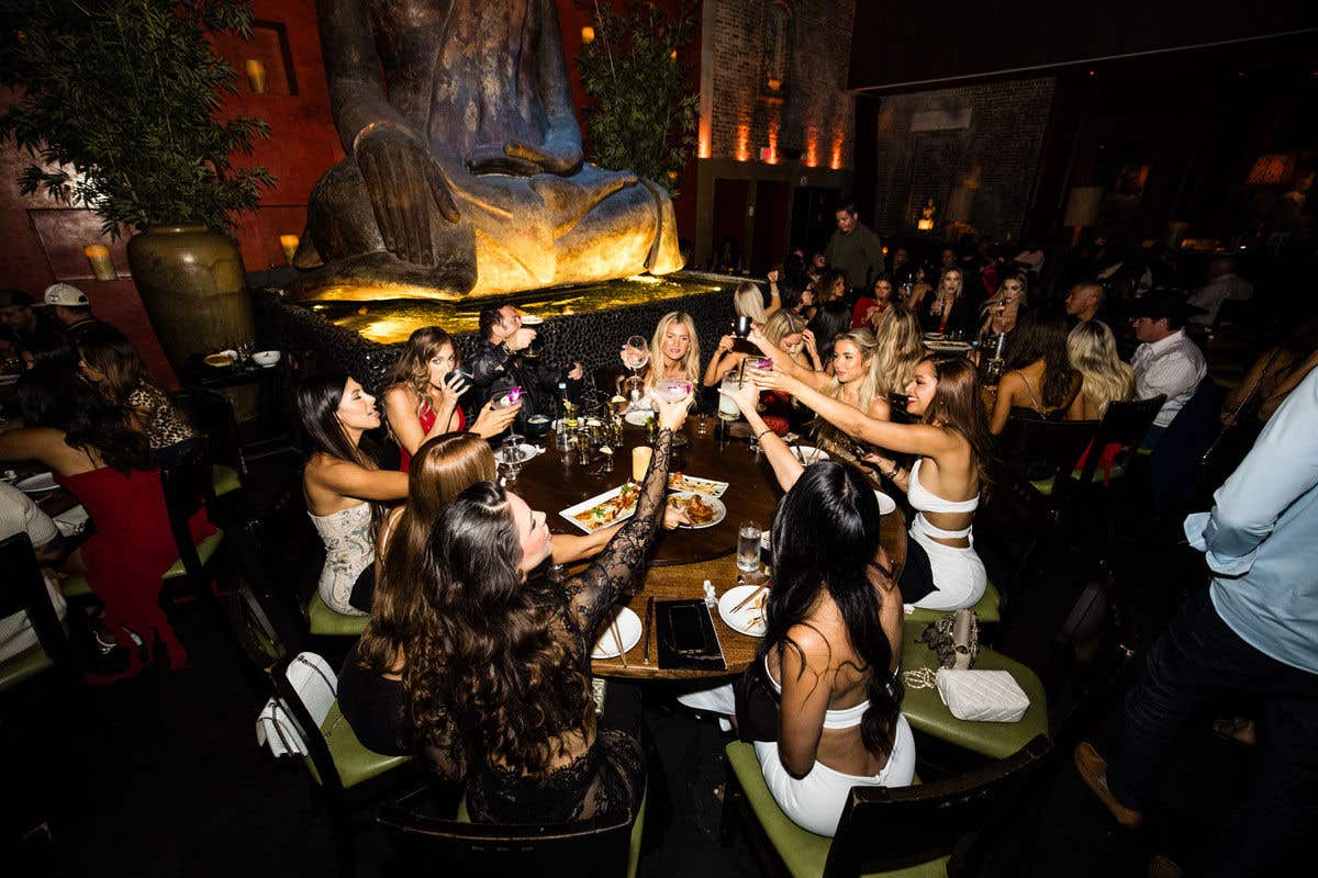 Group of ladies sitting around a round table toasting their glasses. 