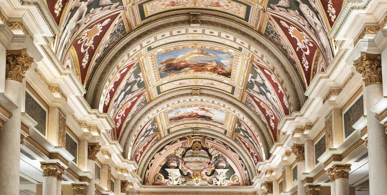 Lavishly decorated vaulted ceiling featuring intricate frescoes and ornate architectural details in a classical style building.