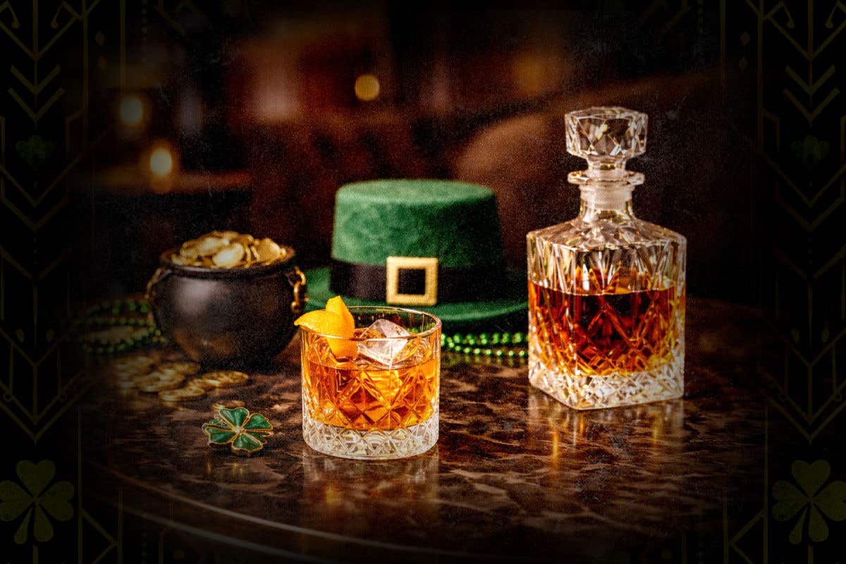 Whiskey shown in a cut crystal rocks glass, with a green leprechaun hat and pot of gold show behind.