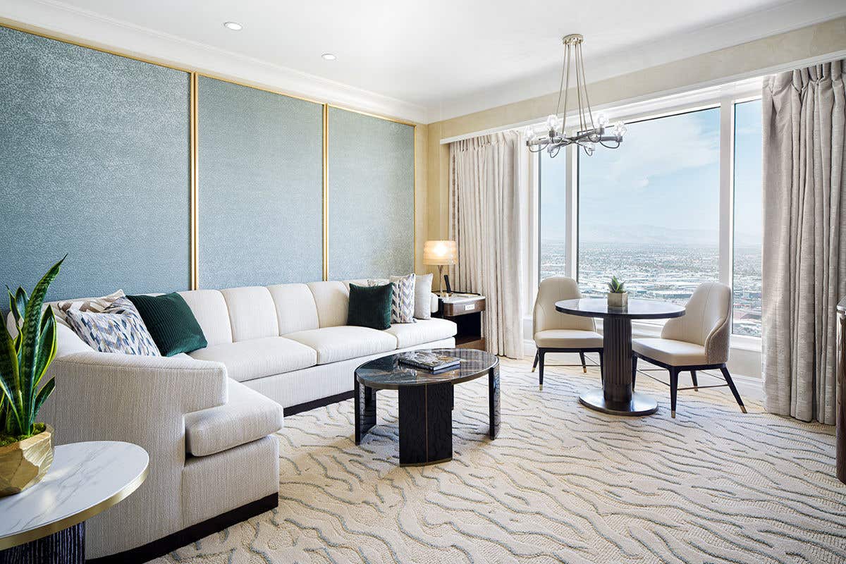 Luxury suite living room with sectional sofa, dining table, and floor-to-ceiling windows overlooking Las Vegas