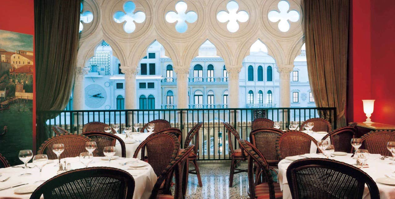 Elegant restaurant with a Venetian-themed decor, featuring arched windows overlooking a balcony and neatly set tables.