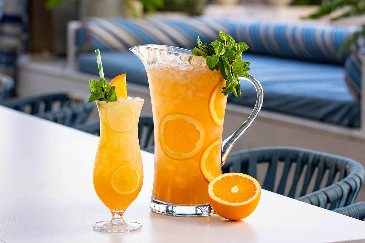 A pitcher and glass of orange punch garnished with mint and orange slices, sitting on an outdoor table.