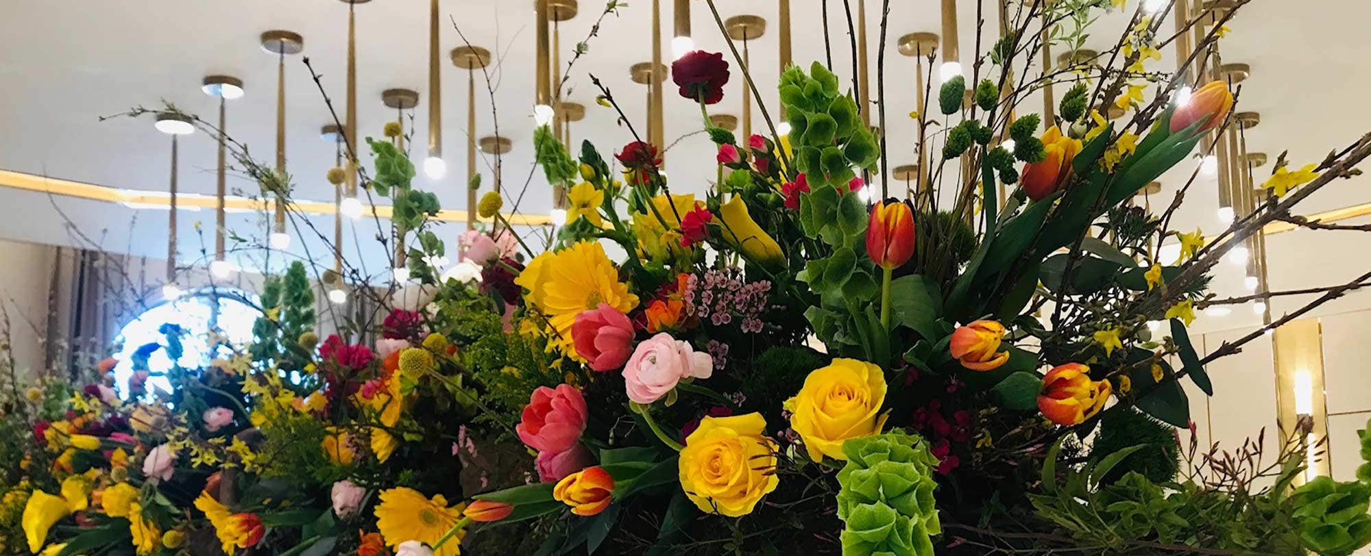 A vibrant floral arrangement with yellow, red, and pink flowers, branches, and greenery under hanging lights.