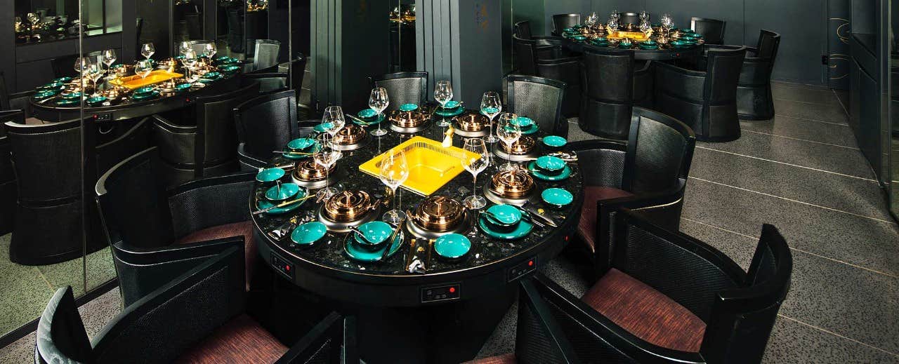 Elegant dining table set with green and gold dishes, surrounded by black chairs, in a modern, dimly-lit room with mirrors.