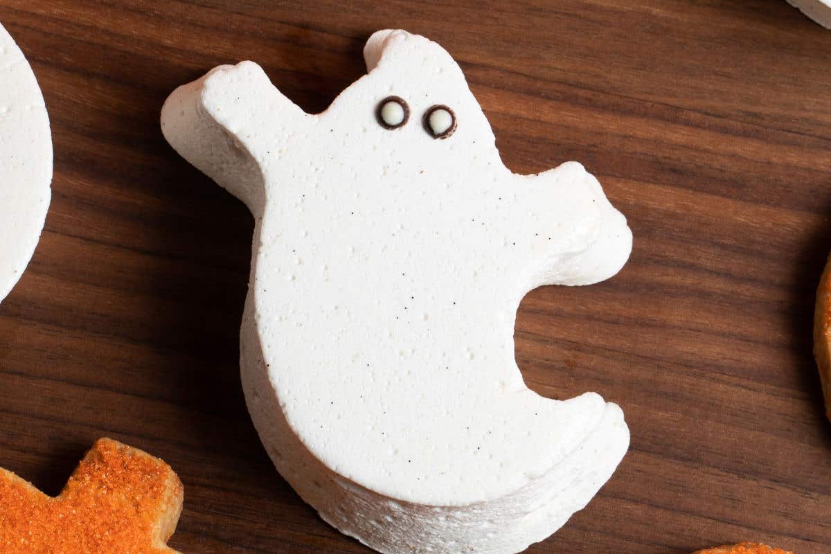Ghost-shaped marshmallow decorated with white icing and chocolate eyes.