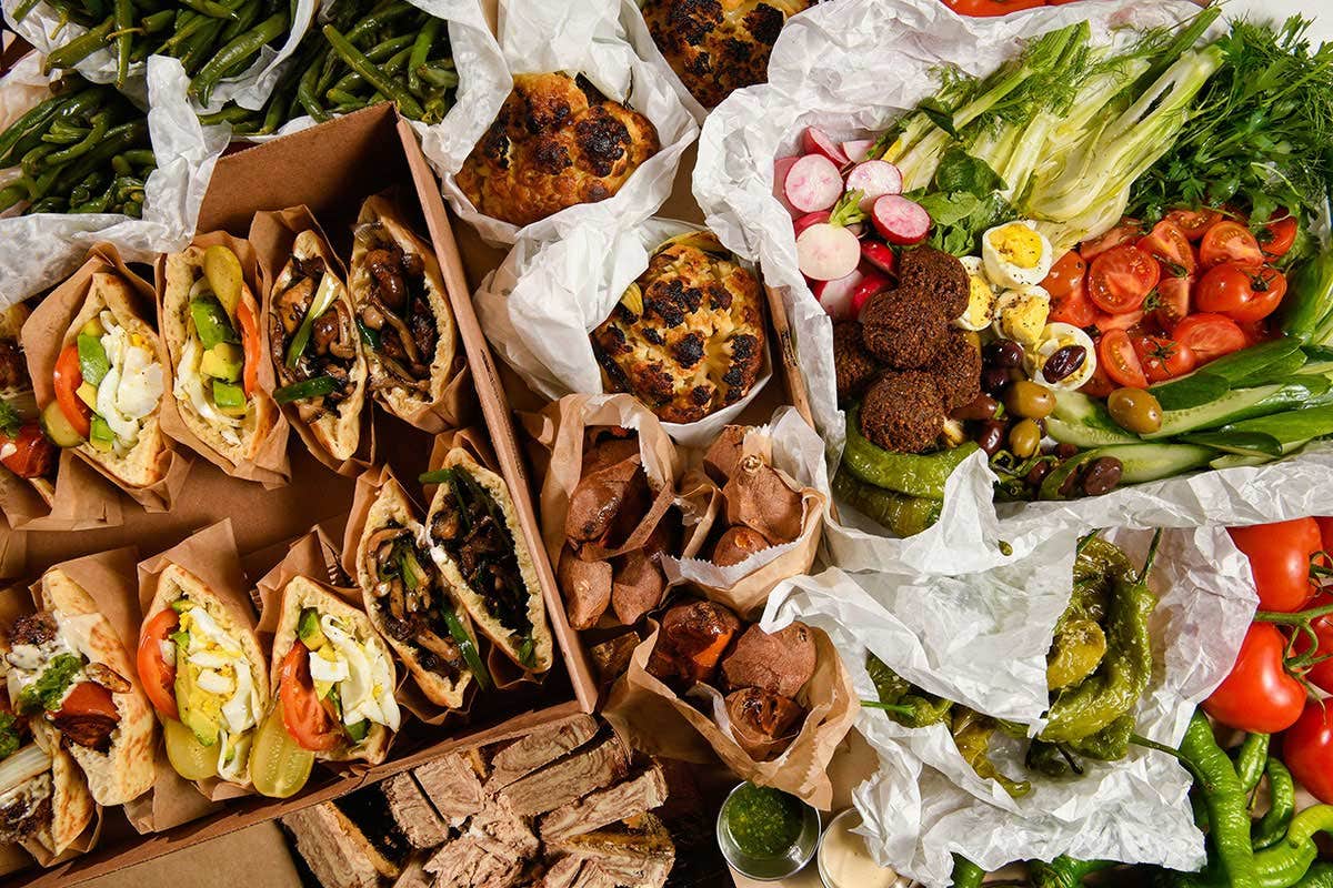 A table filled with assorted Mediterranean foods, including pita sandwiches, salads, vegetables, olives, and bread.