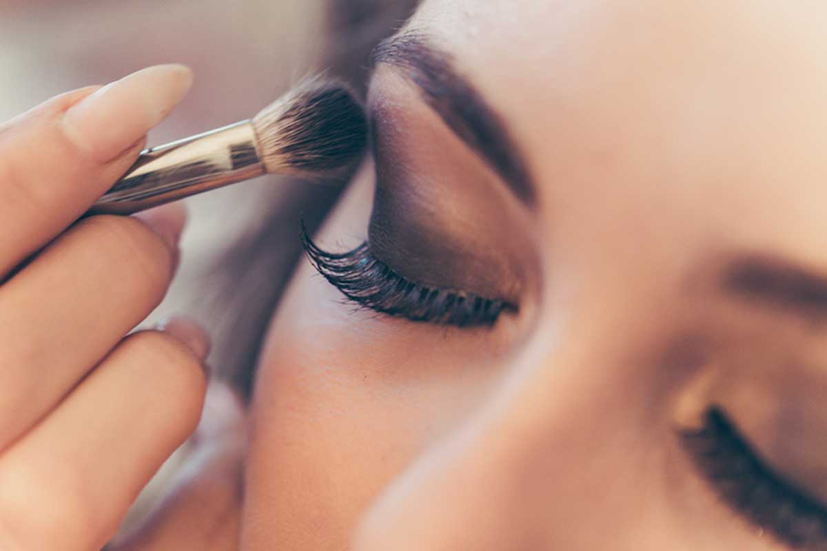 A close up of a woman’s face with makeup being applied to the eyes.