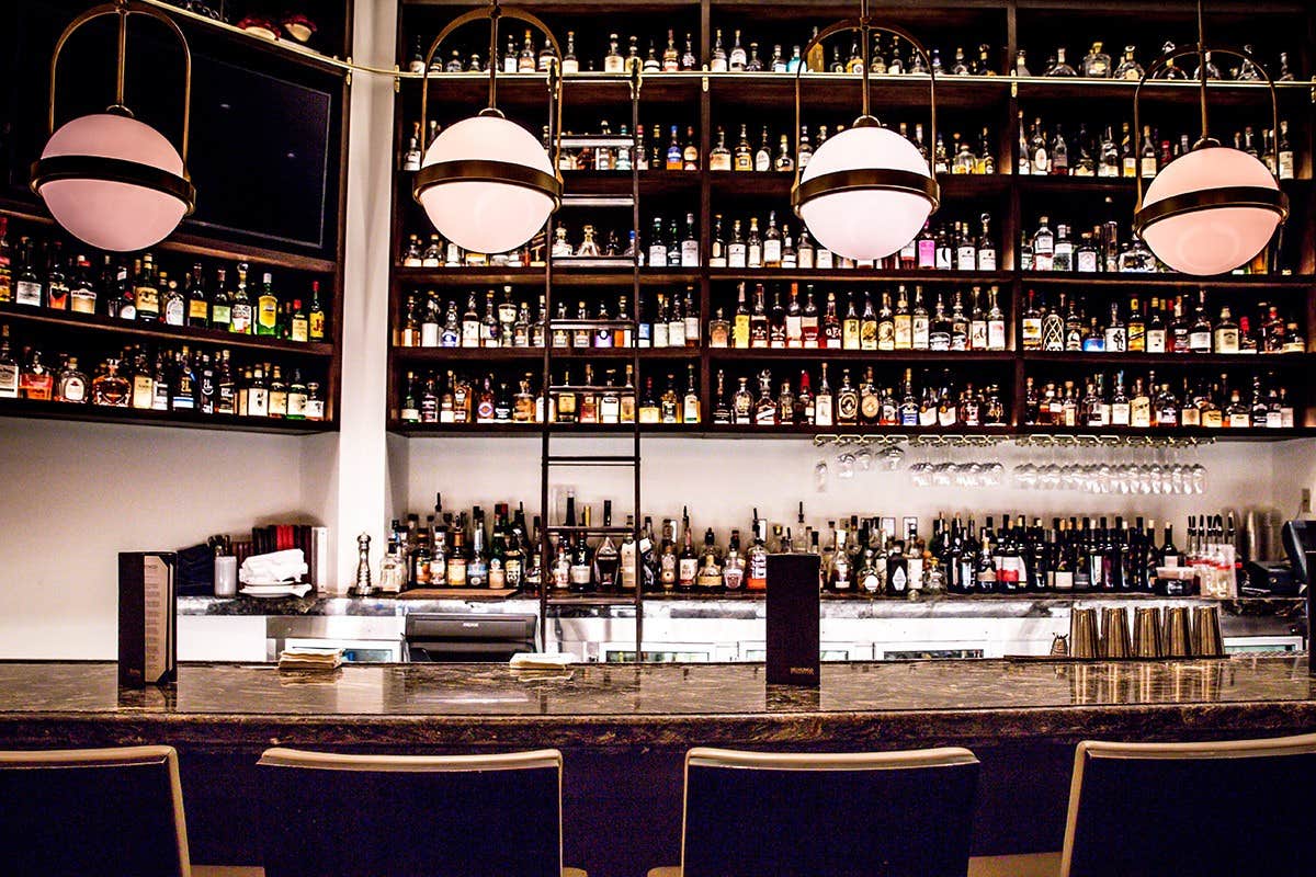 A well-stocked bar with many liquor bottles, three spherical pendant lights, and a row of chairs in front of the counter.