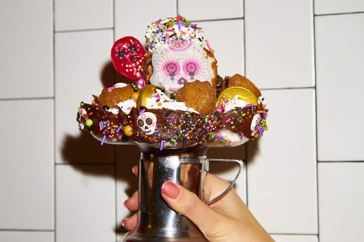 Over-the-top milkshake topped with candy, cookies, sprinkles, and sugar skull decorations.