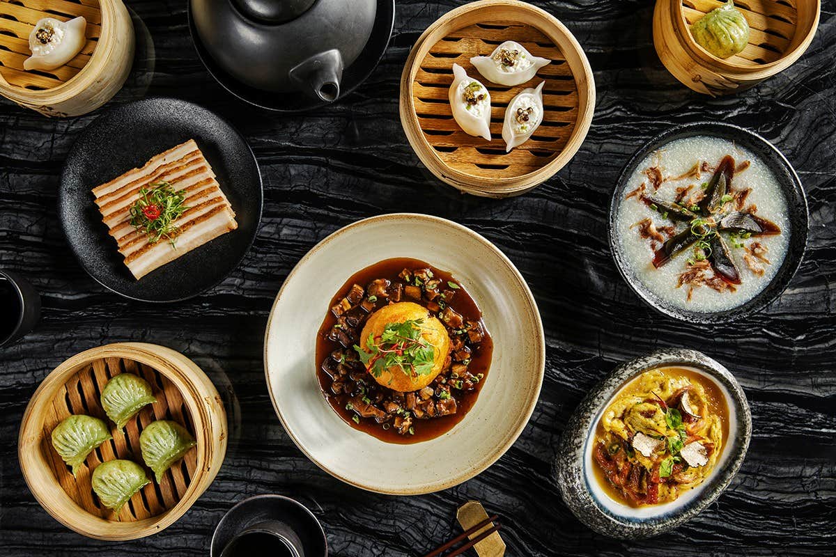 An overhead view of various dim sum dishes, including dumplings, buns, and porridge served on a marble table.