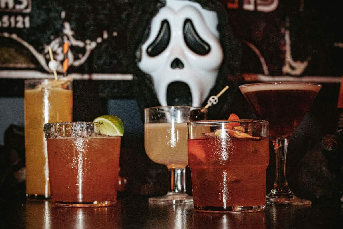 Halloween-themed cocktails arranged on a table with a Ghostface decoration in the background.