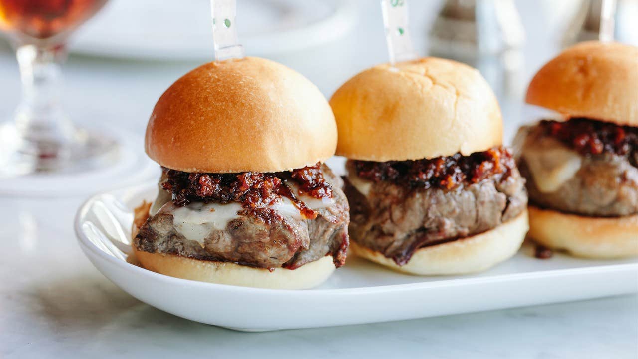 Three beef sliders with melted cheese and caramelized onions in buns on a white plate.