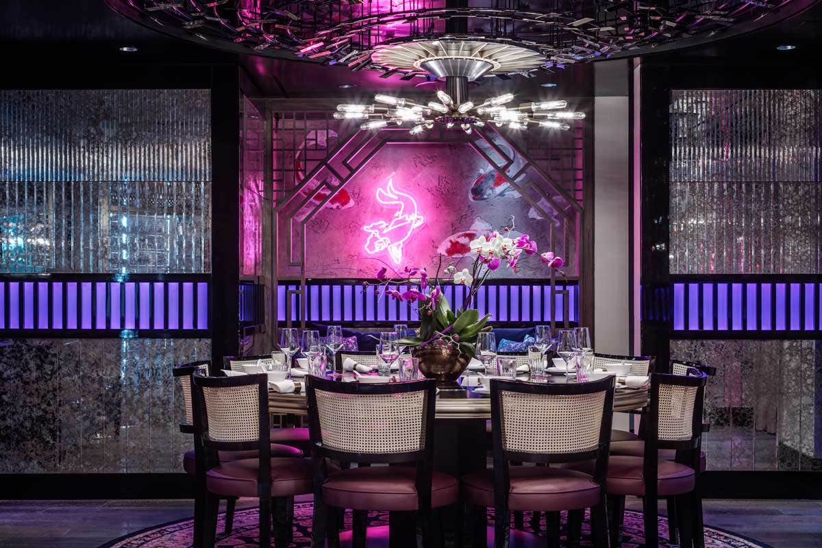 Elegant restaurant interior with neon pink lights, modern chandelier, and a round dining table set for eight.