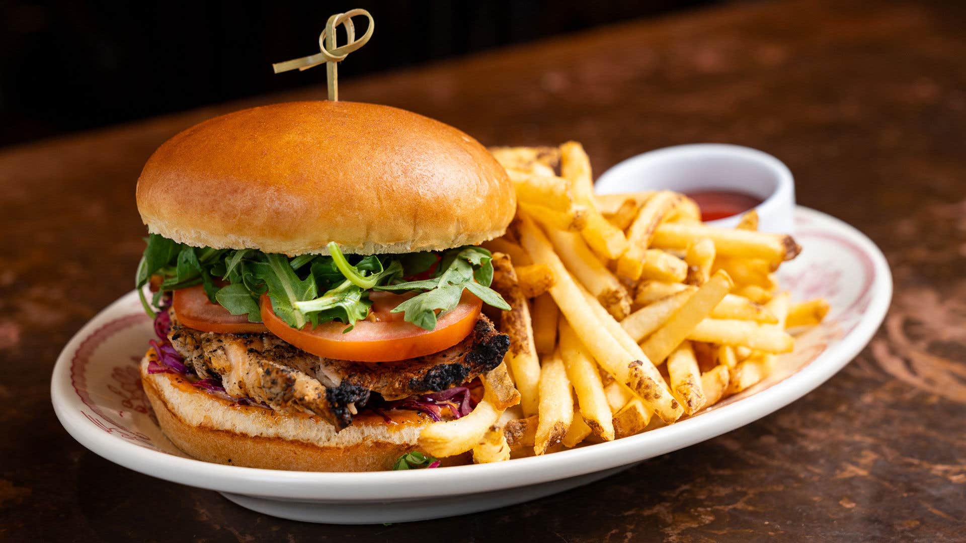 Grilled chicken sandwich with arugula and tomato, served with French fries and a cup of ketchup.