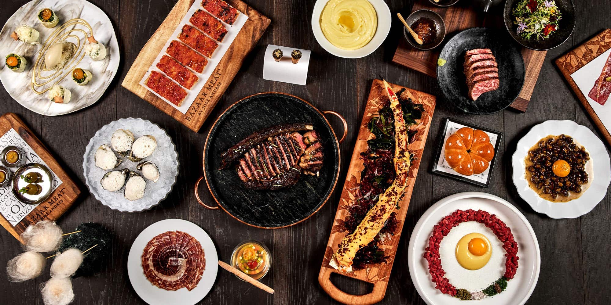 Overhead view of an upscale culinary spread with steak, seafood, oysters, and artfully plated dishes.