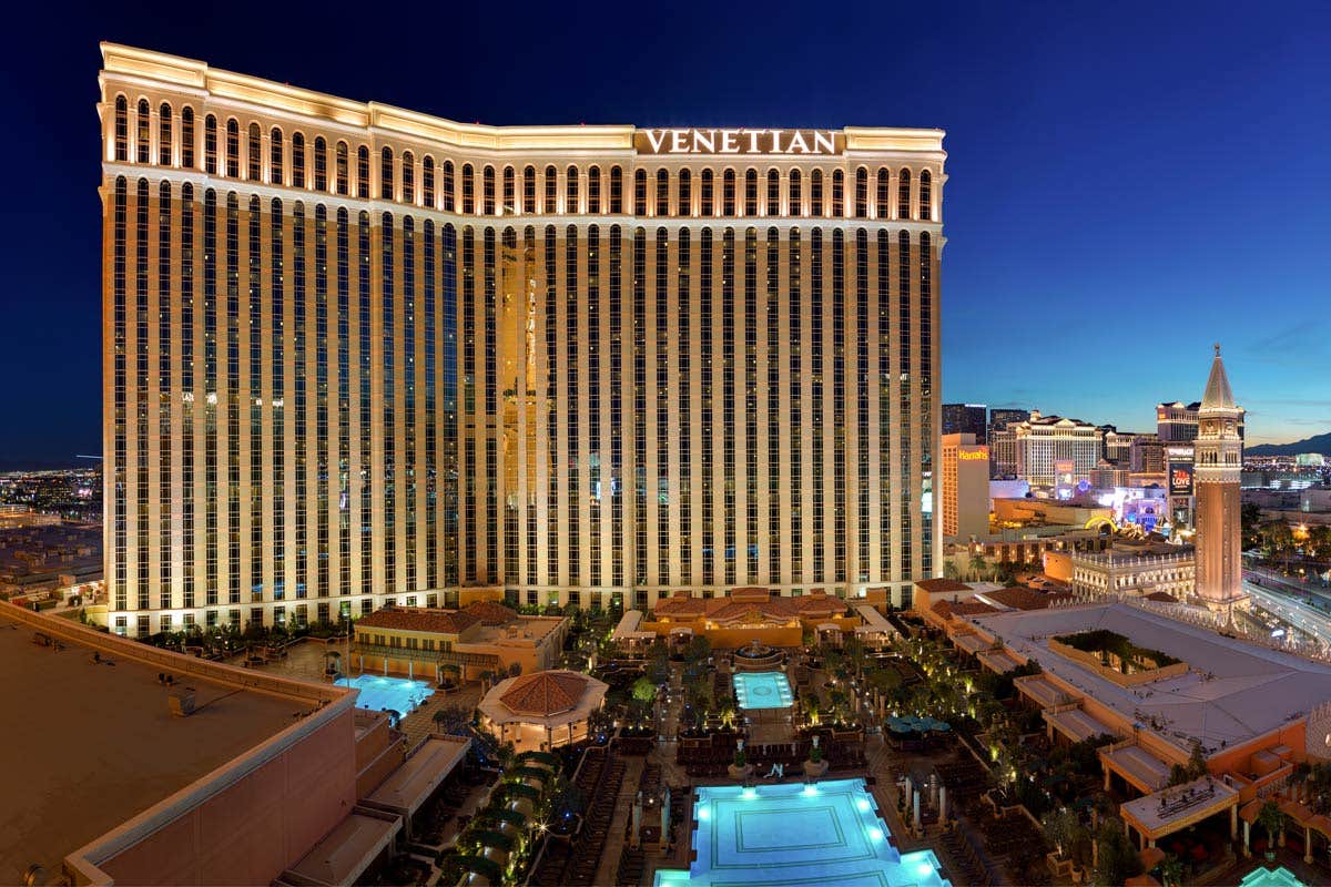 The Venetian hotel and casino in Las Vegas illuminated at night, with pools and surrounding buildings also lit up.