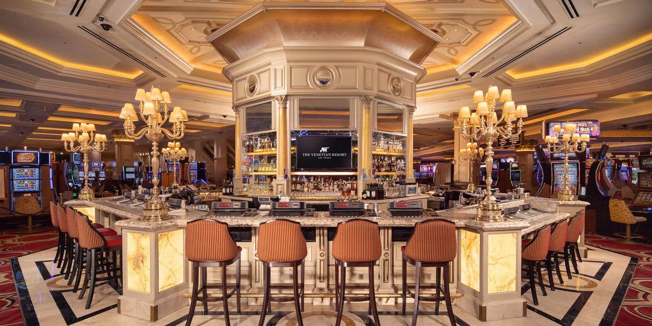 Bellini Bar with marble top, surrounded by plush barstools, chandeliers, and slot machines in the background.