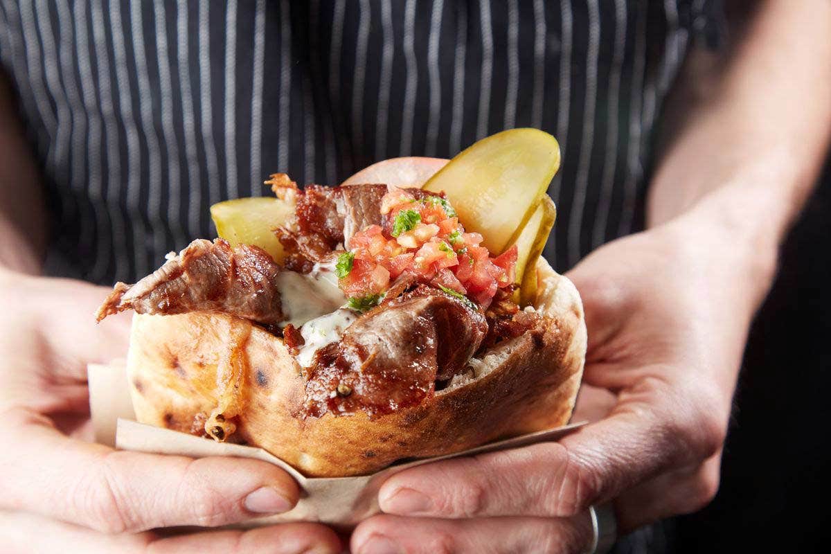 Close-up of hands holding a pita filled with grilled meat, pickles, and salsa.