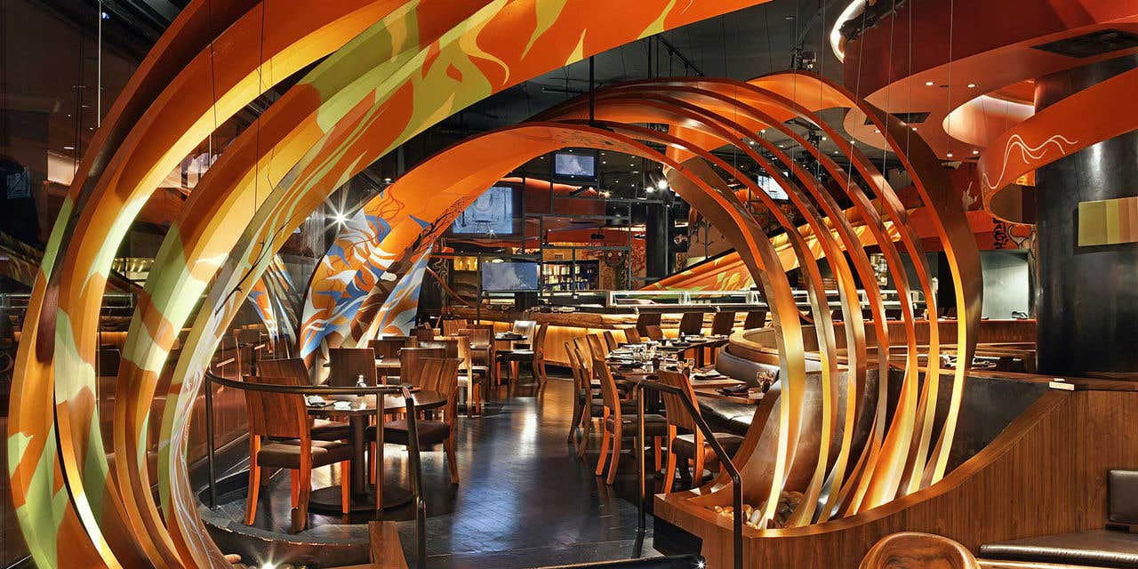 Modern restaurant with an artistic orange and yellow circular archway, wooden tables, and ambient lighting.