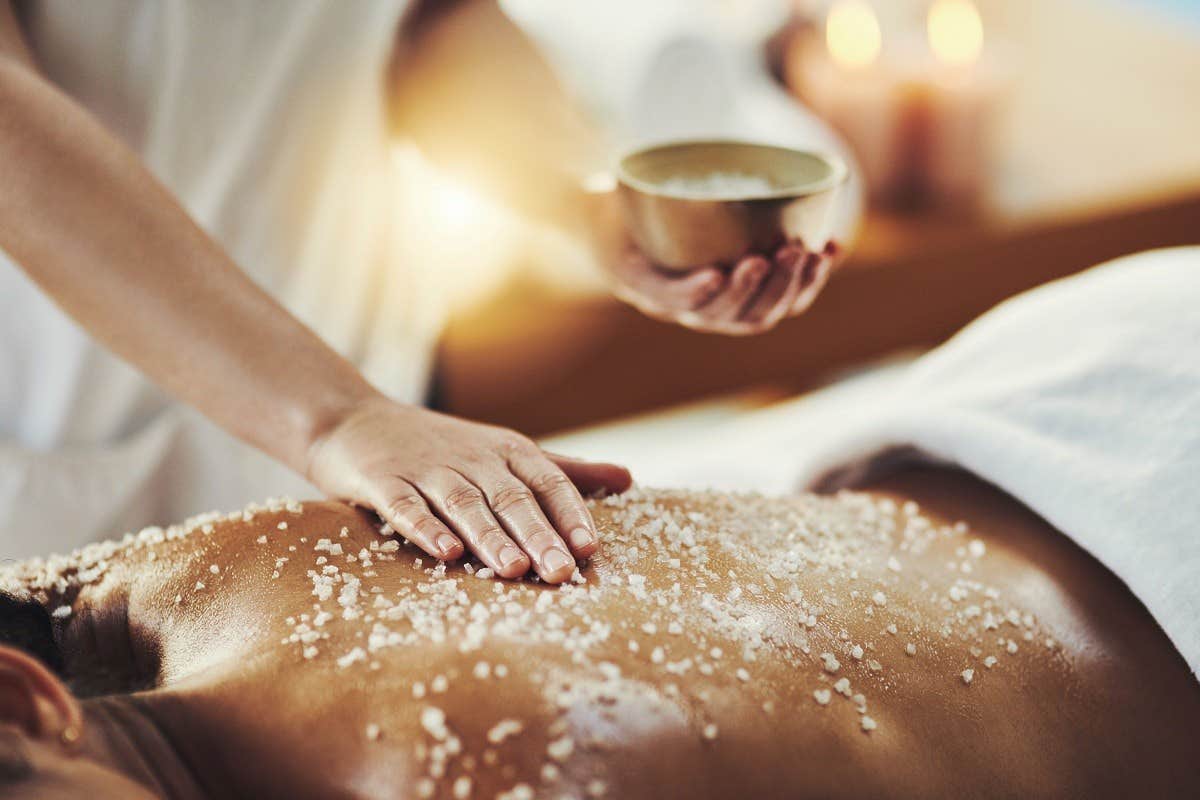 Person receiving a back massage with sea salt treatment in a serene spa setting, with candles in the background.