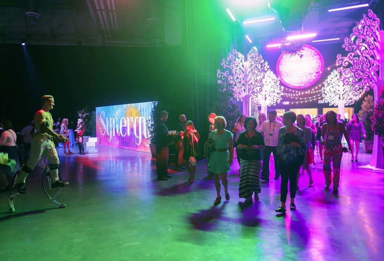 Interior of expo hall c during an event, with green and purple lights and people mingling.