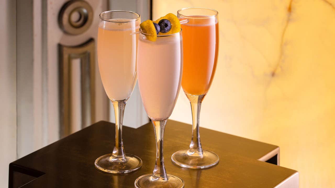 Three elegant champagne flutes filled with colorful cocktails, garnished with lemon twists, on a brown surface.