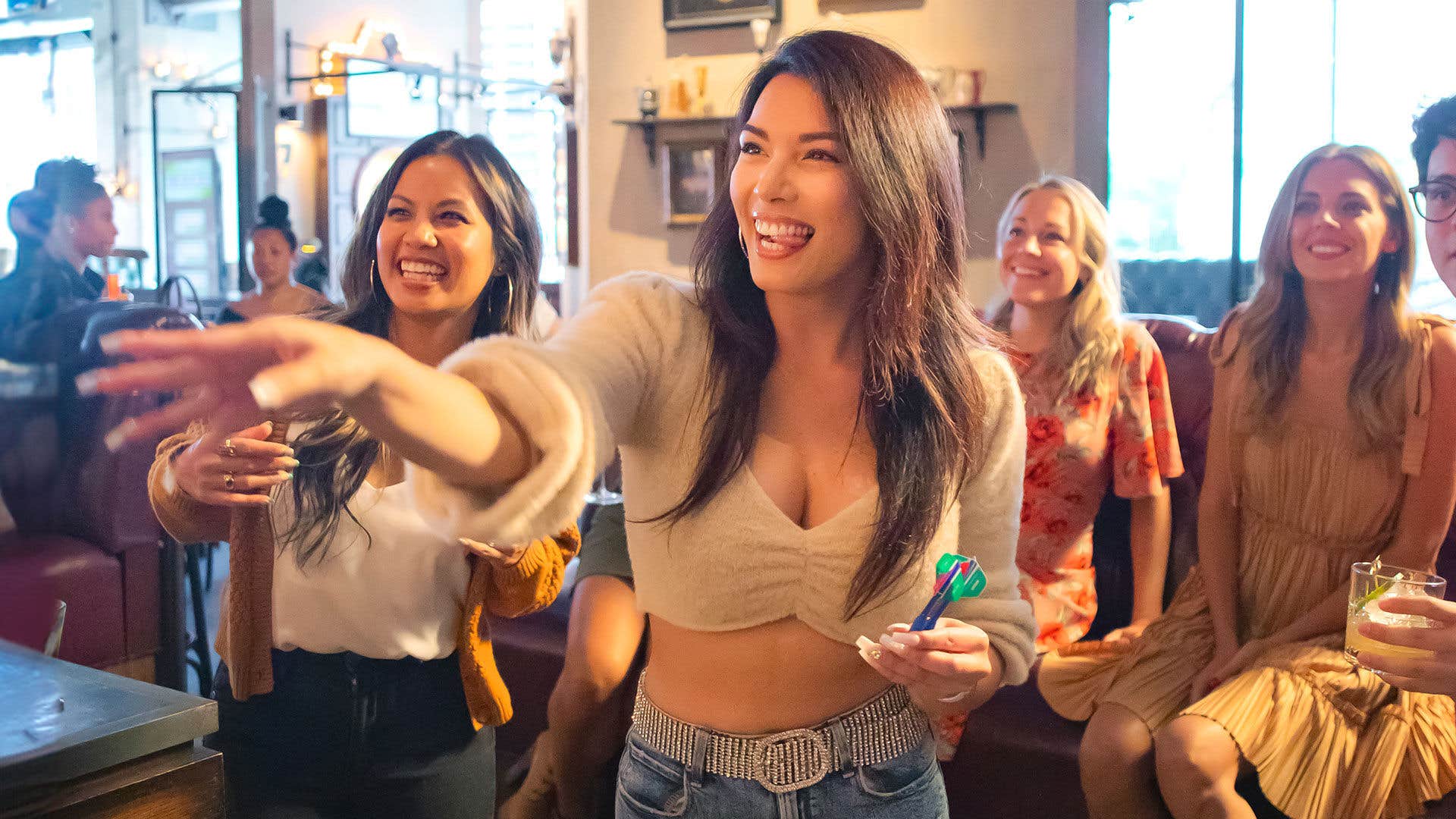 A group of guests playing darts in a bar watching and smiling.